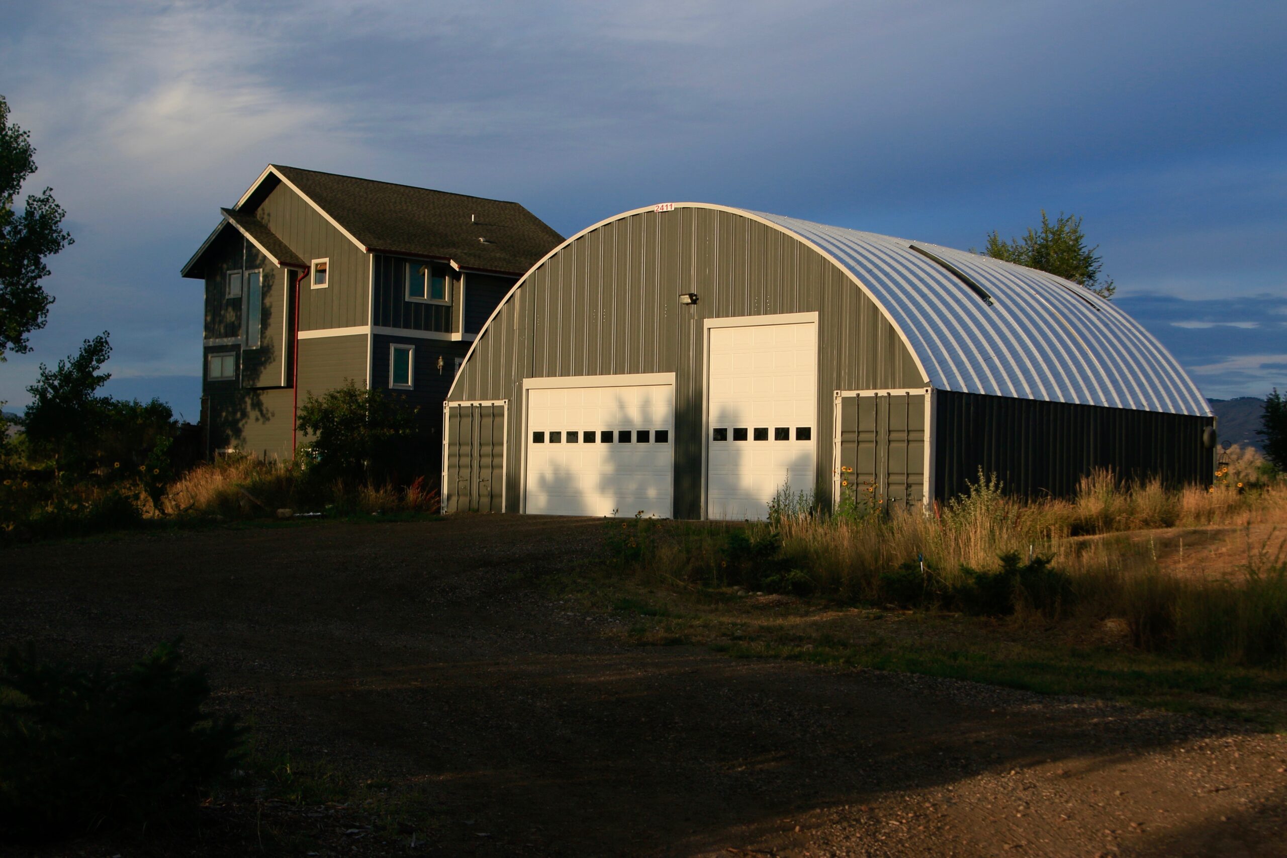 large shipping container building with forest green endwalls, white garage doors and arch roof