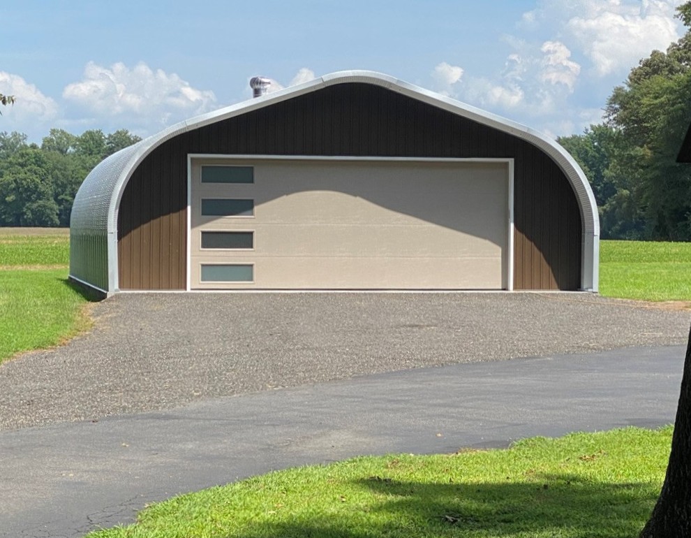 A-Model Quonset hut with custom brown end wall, large tan garage door with four horizontal windows, and a rotating ventilation system on top.