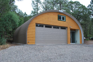 S-Model Quonset hut with custom end wall made from logs, a gray garage door. and a sliding door on the right.
