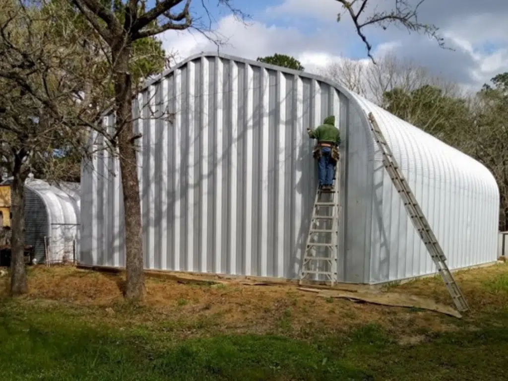 Person on ladder leaning against the steel back endwall of an A-model Quonset building.