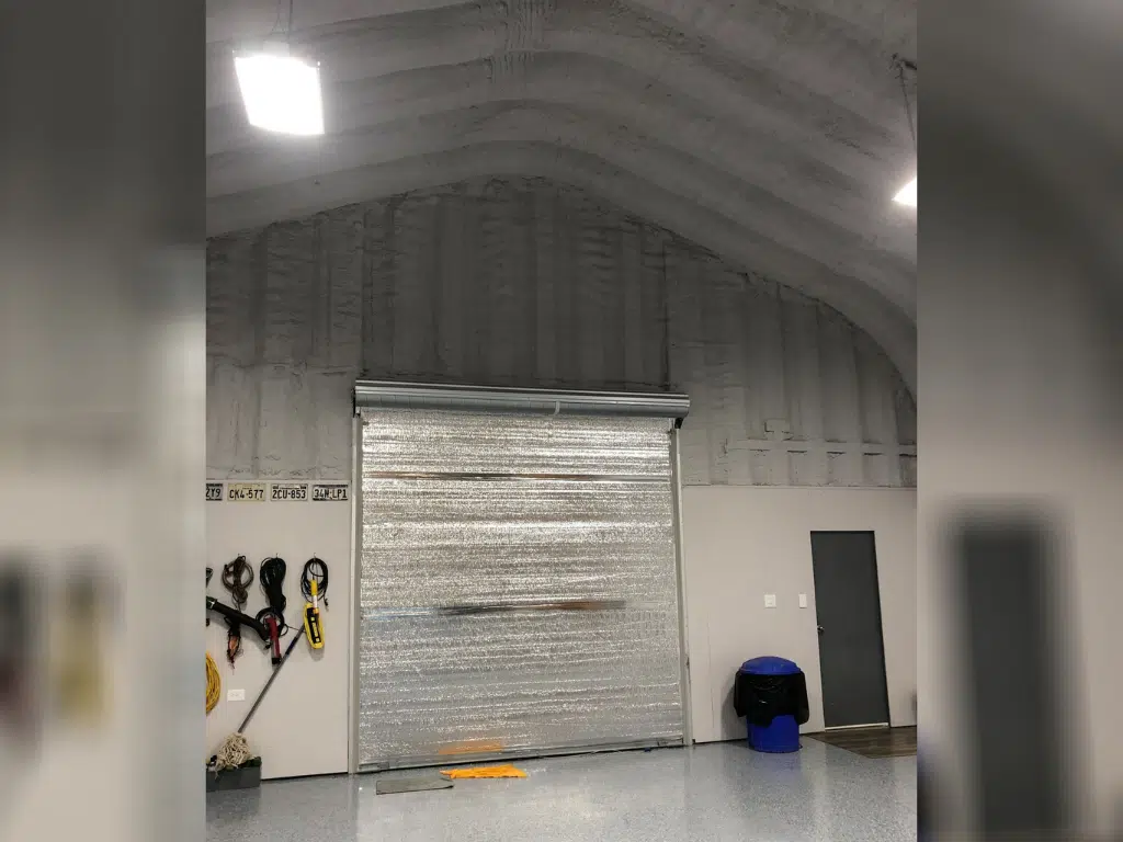 Inside A-model Quonset hut, tools hanging on wall, rolling door, and grey front entrance door.