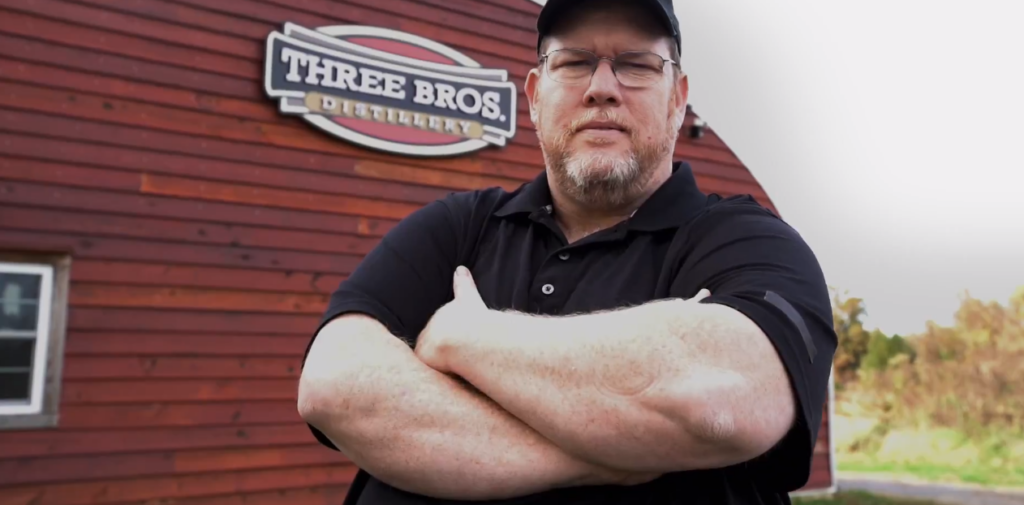 Dave Reavis standing outside of his Quonset Hut Distillery with a custom red wood endwall.