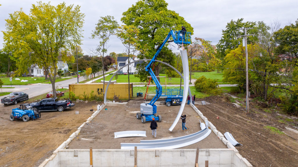 Workers on lift and ground moving arch piece into place.