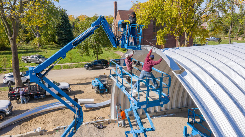 Workers on two lifts piecing together metal arches.