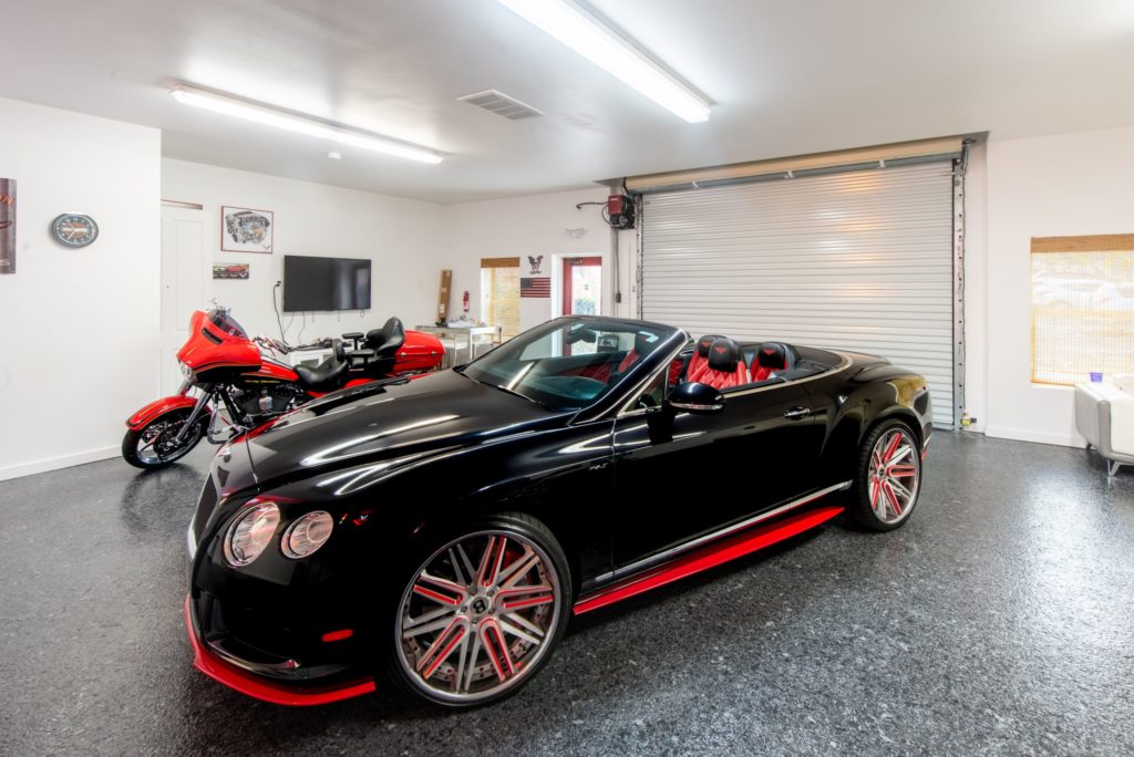 Inside of Quonset home garage, red trimmed black convertible, red and black motorcycle, rolling door, glass entrance door